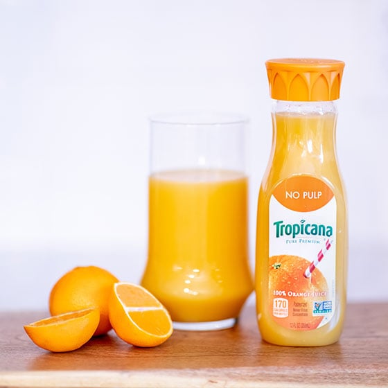 Tropicana orange juice next to a glass of orange juice and oranges